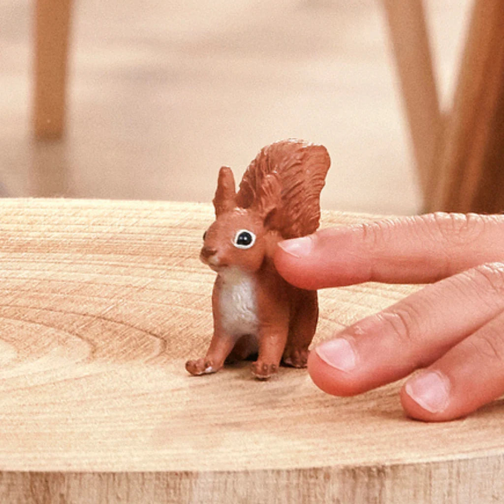 Schleich Squirrel figure beside fingers on a wooden surface