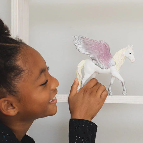 Child holding the Schleich Sunrise Pegasus figure on a white shelf