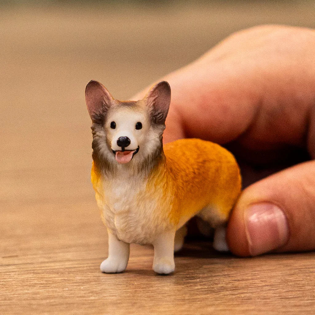 A hand beside the corgi figurine highlighting its size, detailed coat, and standing pose.