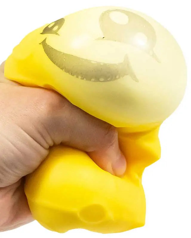 Scrunchems Squeezy Cheese being squeezed by hand with the yellow squishy body bulging outward above the grip