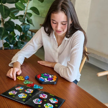Person at a table with SmartGames IQ Pentagon board, loose pieces and open booklet pages