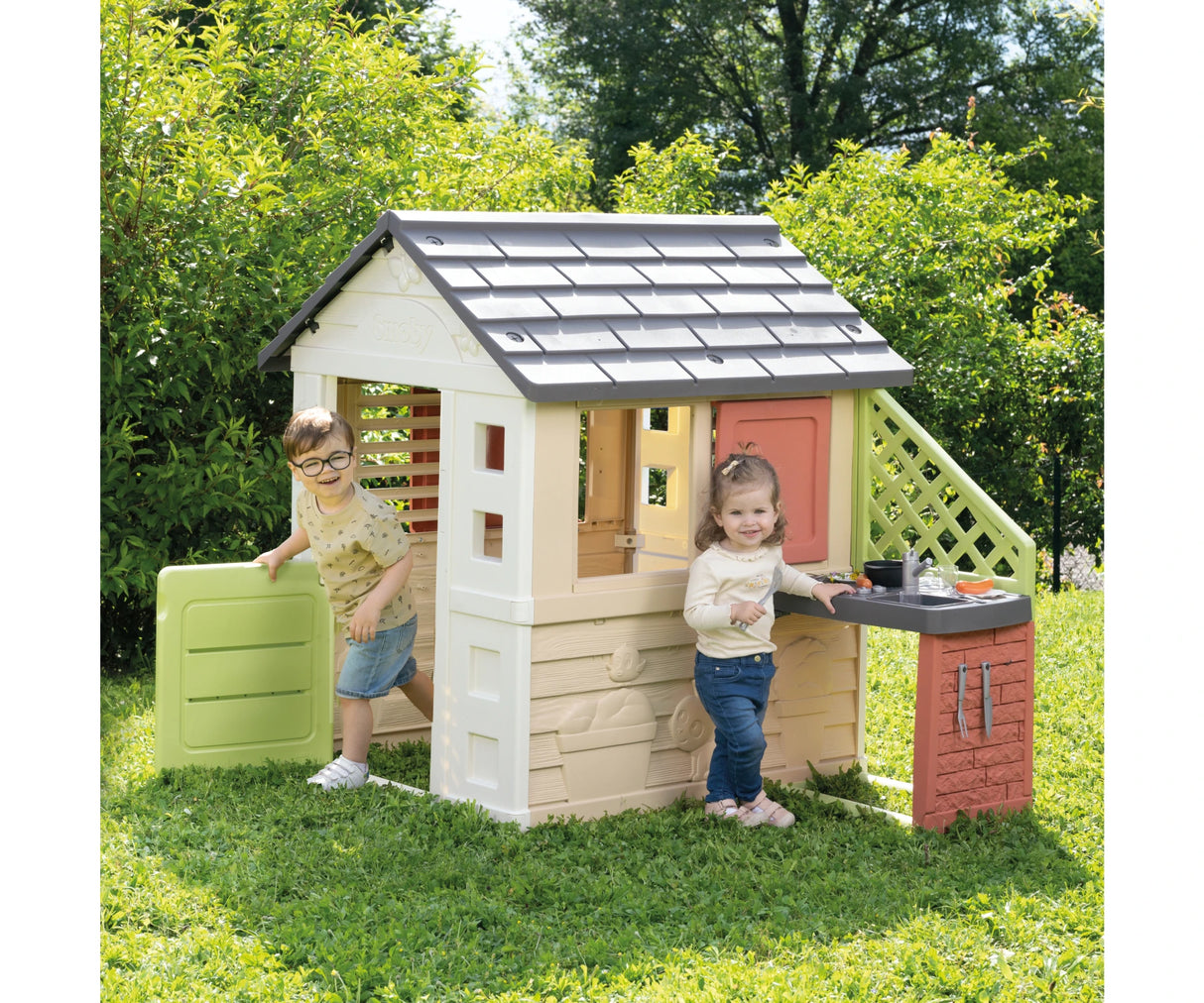 Two children beside the Smoby Life Nature Playhouse with attached kitchen in a garden