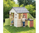 Two children beside the Smoby Life Nature Playhouse with attached kitchen in a garden