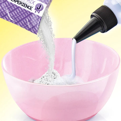 White slime powder and liquid being poured from a purple sachet and nozzle bottle into a pink mixing bowl against a yellow background.