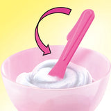 Pink spatula stirring white slime in a pink mixing bowl, with a curved pink arrow indicating the mixing motion against a yellow background.