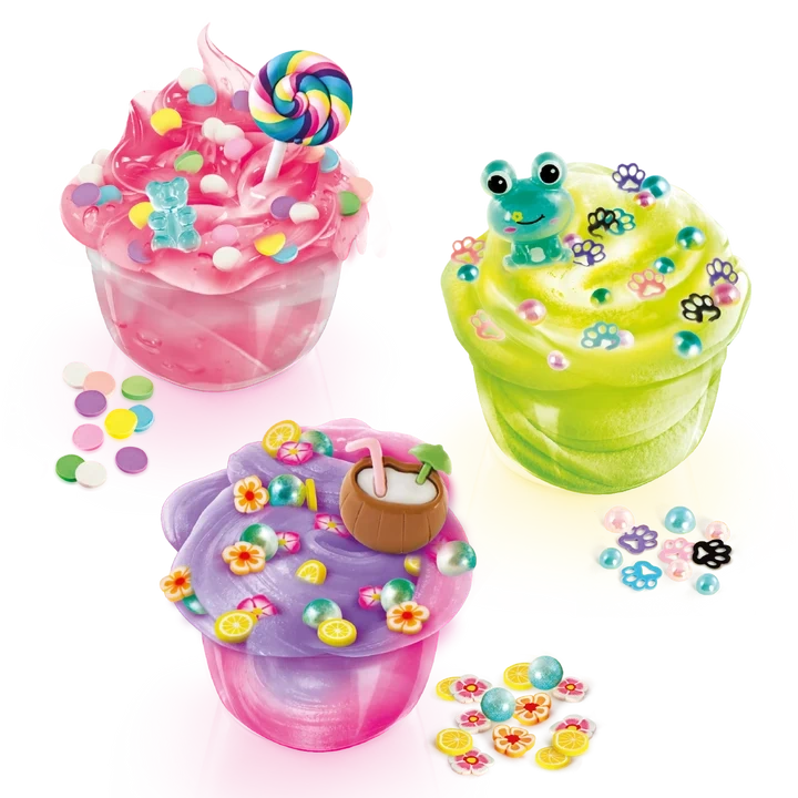 Three decorated So Slime Pop Style creations in clear pots: pink slime topped with a rainbow lollipop and sweets, green slime with a frog charm and paw prints, and purple slime with a coconut drink decoration.