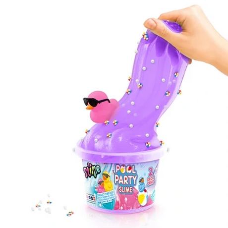 Hand stretching purple slime upwards from a So Slime Pool Party bucket, with a pink duck wearing black sunglasses resting in the slime alongside colourful decorations and white foam beads.