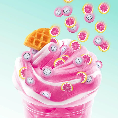 Close-up of pink and white swirled So Slime in a clear pot, decorated with miniature dragon fruit and pink grapefruit slices and a waffle shaped charm against a pale turquoise background.