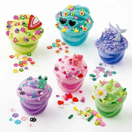 Six colourful So Slime creations in clear pots, decorated with miniature sweets, flowers, heart shaped sunglasses, a frog charm, pink hearts and a blue mermaid tail, with loose decorations scattered around them.