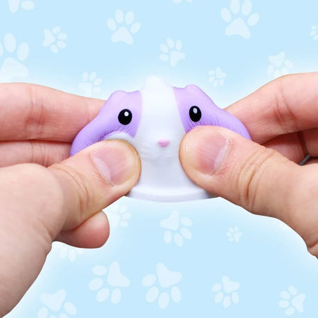 Close-up of two hands squeezing a purple and white animal squishy figure with black eyes and a pink nose, against a pale blue background decorated with paw prints.