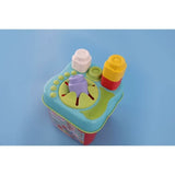 Soft Clemmy Sensory Bucket photographed from above on a blue background, showing white, yellow, green and purple blocks inserted into the turquoise lid's stacking studs and flower shaped opening.