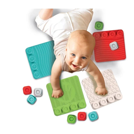 Baby wearing a white outfit crawling across the Soft Clemmy Sensory Path, with hands resting on green and white textured tiles surrounded by colourful soft blocks.