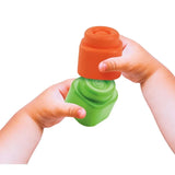 Close-up of a child's hands stacking an orange Soft Clemmy block onto a green block against a white background.