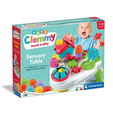 Clementoni Soft Clemmy Touch & Play Sensory Table retail packaging showing the colourful activity table, baby holding a red hammer, 10 soft blocks included and 10 to 36 months age marking.