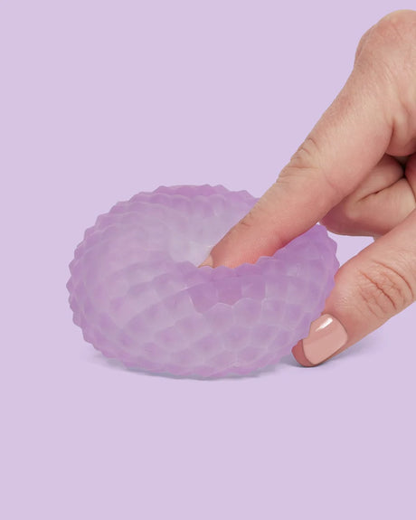 Speks Gump Surface Scale Mist squishy being pressed by hand, showing the purple raised scale texture