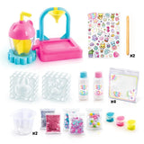 Squish Squish DIY Squishy Factory contents arranged on a white background, including the pink mixing machine, bunny and paw moulds, two gel bottles, three coloured dyes, mixing cups, wooden sticks, glitter, confetti, pom poms, printed bags and sticker sheet.