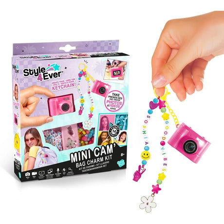 Style 4 Ever Mini Cam Bag Charm Kit retail box displayed beside a pink mini digital camera hanging from a yellow clip with colourful letter beads, hearts, stars, a smiley face and flower charms.