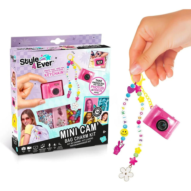 Style 4 Ever Mini Cam Bag Charm Kit retail box displayed beside a pink mini digital camera hanging from a yellow clip with colourful letter beads, hearts, stars, a smiley face and flower charms.