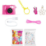 Style 4 Ever Mini Cam Bag Charm Kit contents showing a pink digital camera, yellow keychain clip, pink cord, USB-C charging cable, flower and hand charms, colourful shaped beads and white alphabet beads.