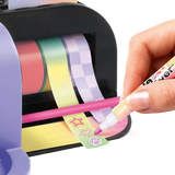 Close-up of a hand using a pink marker to decorate adhesive tape printed with stars, a sun and paw print, with pink, green and purple tape rolls mounted inside the Style 4 Ever Scrapbooking Studio Pro.