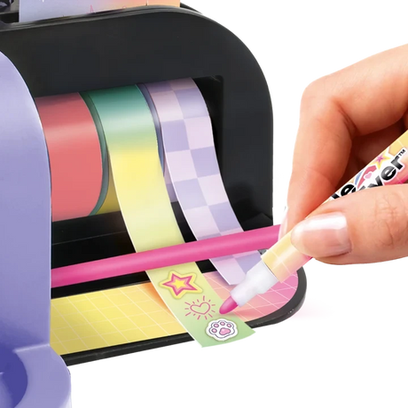 Close-up of a hand using a pink marker to decorate adhesive tape printed with stars, a sun and paw print, with pink, green and purple tape rolls mounted inside the Style 4 Ever Scrapbooking Studio Pro.