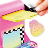 Close-up of the pink Style 4 Ever Scrapbooking Studio Pro embossing machine with a yellow embossing plate and black turning handle, alongside a pastel coloured bunny face decoration with raised details.