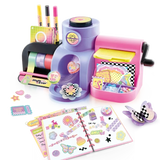 Assembled Style 4 Ever Scrapbooking Studio Pro showing colourful tape rolls, three markers, pink embossing machine, yellow plate and craft storage compartments, with an open decorated scrapbook, raised stickers and paper flower decorations in front.