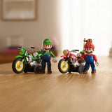 Mario and Luigi figures standing beside their red and green motorcycles on a wooden tabletop, with both motorcycles positioned behind the figures.