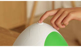 Close-up of a finger pressing the white button at the top of the closed Yoshi egg, showing its textured white shell and large green spot.