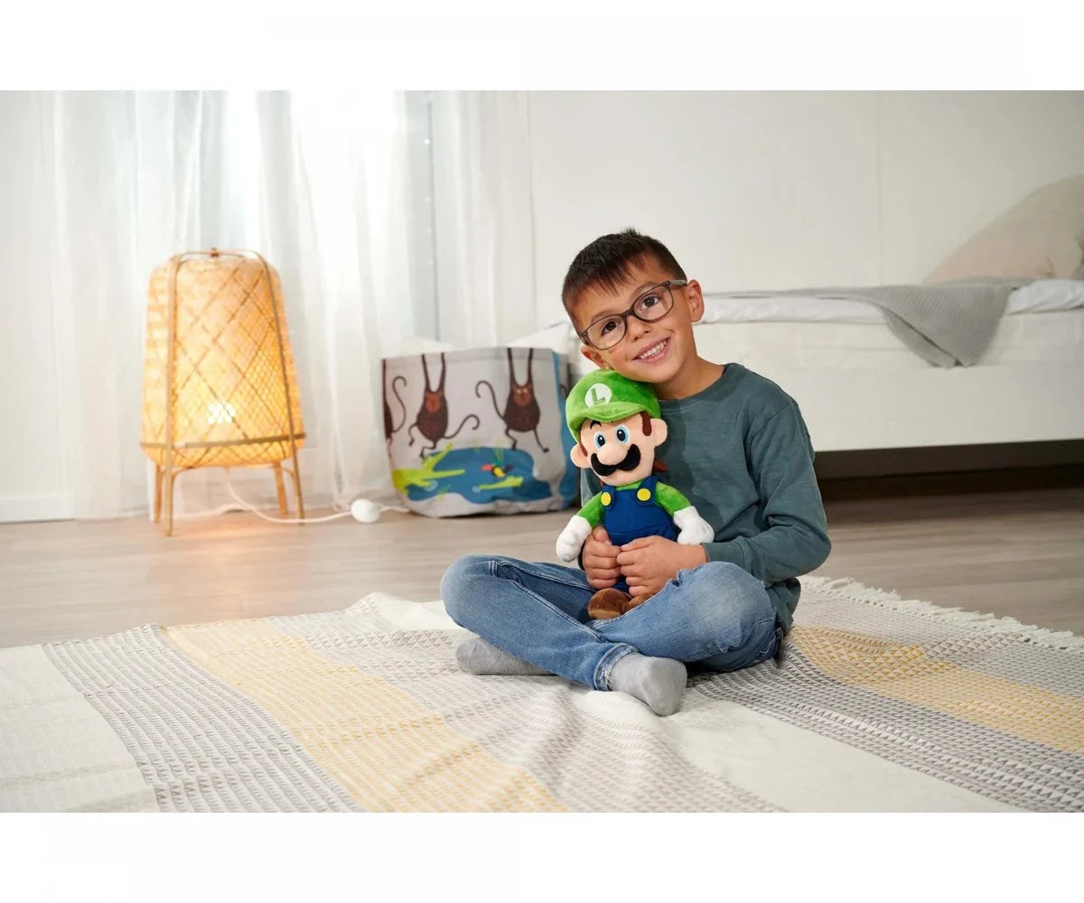 Child sitting cross-legged on a rug holding a Super Mario Luigi plush toy up to their face, showing the toy's size relative to a school-age child