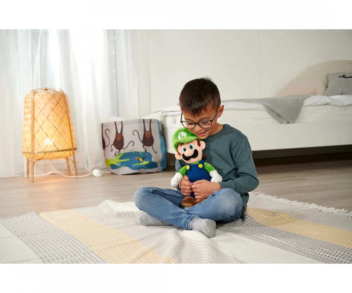 Child seated on a bedroom floor looking down at a Super Mario Luigi plush soft toy held in both hands, showing the toy held.