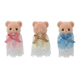 Three Sylvanian Families Biscuit Bear baby figures standing separately against a white background, wearing pink, yellow and blue lace gowns with large matching bows. The middle baby has closed eyes.
