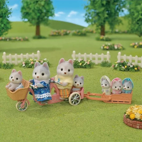 Husky Family outdoor play scene with parents cycling and triplets riding in sleigh trailer on grassy field in Ireland.