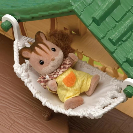 Small brown Sylvanian Families animal figure wearing yellow dungarees reclining in the white woven hammock at the Lakeside Lodge.