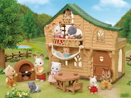Sylvanian Families Lakeside Lodge with animal figures on the balcony, a baby in the hammock and figures beside the wooden table and brick stove.