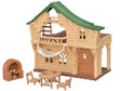 Sylvanian Families Lakeside Lodge log cabin with green roof, hanging white hammock, brick stove, wooden table and two chairs on a white background.