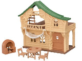 Sylvanian Families Lakeside Lodge log cabin with green roof, hanging white hammock, brick stove, wooden table and two chairs on a white background.