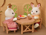 Two Sylvanian Families rabbit figures sitting at the Lakeside Lodge wooden table with a plate of fruit and miniature cups.