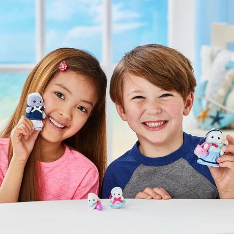 Smiling girl and boy holding Sylvanian Families Seal Family parent figures, with the two miniature baby seals displayed on the table between them.