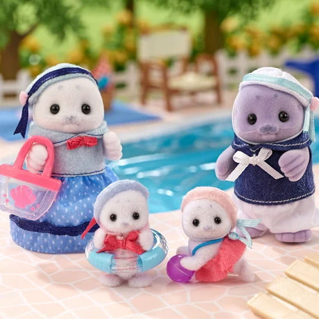 Four Sylvanian Families Seal Family figures arranged beside a swimming pool, showing their blue and pink sailor outfits, pink beach bag, transparent blue swimming ring and purple beach ball.