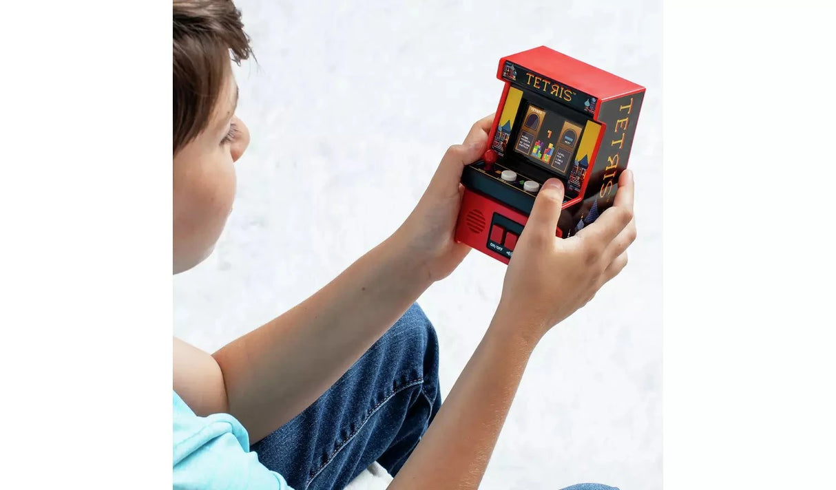 Child holding and playing the Tetris Classics Retro Mini Arcade Machine with both hands, showing the compact size of the red cabinet with colour screen displaying Tetris gameplay