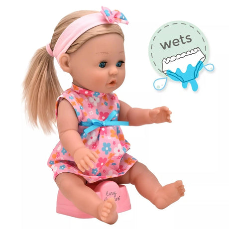 Tiny Tears Classic doll sitting on the pink potty in her floral dress with long blonde hair, with a wetting feature graphic beside her