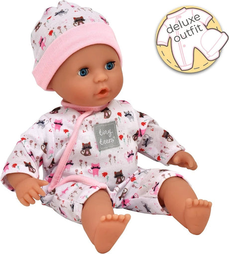Tiny Tears Teeny Baby sitting in a white cat print all in one outfit with pink trim and matching hat, with a deluxe outfit feature graphic