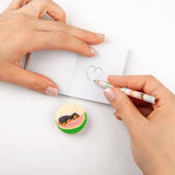 Hands drawing a heart in a small notebook with a TOPModel pencil and round illustrated accessory