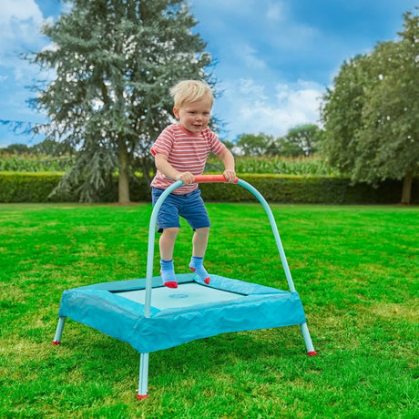 TP Junior Trampoline with child standing on the blue padded mat and holding the handlebar