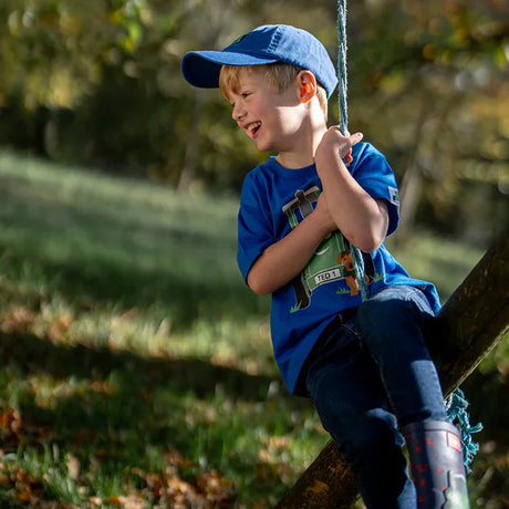 Child wearing blue Tractor Ted cap sitting outdoors on rope swing