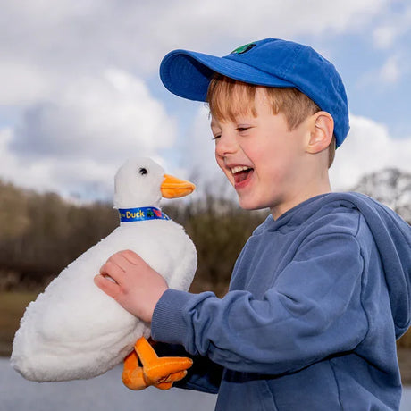 Child holding Tractor Ted Dibble The Duck Soft Toy showing white plush duck with orange beak and blue ribbon collar