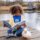 Child sitting by a pond reading the Tractor Ted Dibbles Digger Day storybook with a soft toy duck


