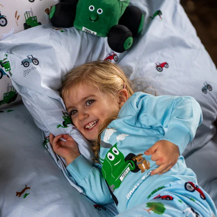 Child lying in bed under blue Tractor Ted & Midge duvet cover featuring green and red tractor print with farm characters