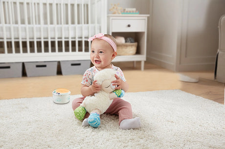 Baby sitting on rug holding VTech 3-in-1 Starry Skies Sheep Soother with electronic module beside them
